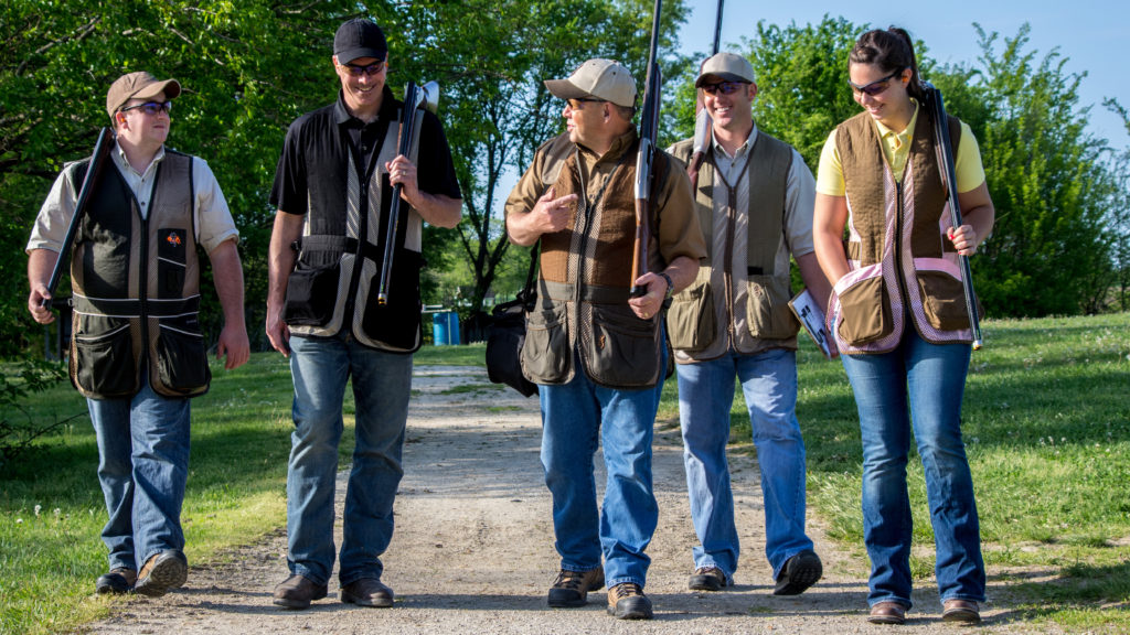 A group of adults talking and walking outside together while carrying shotguns